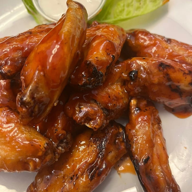 A close-up of several glossy, orange-glazed chicken wings on a white plate with a side of ranch.