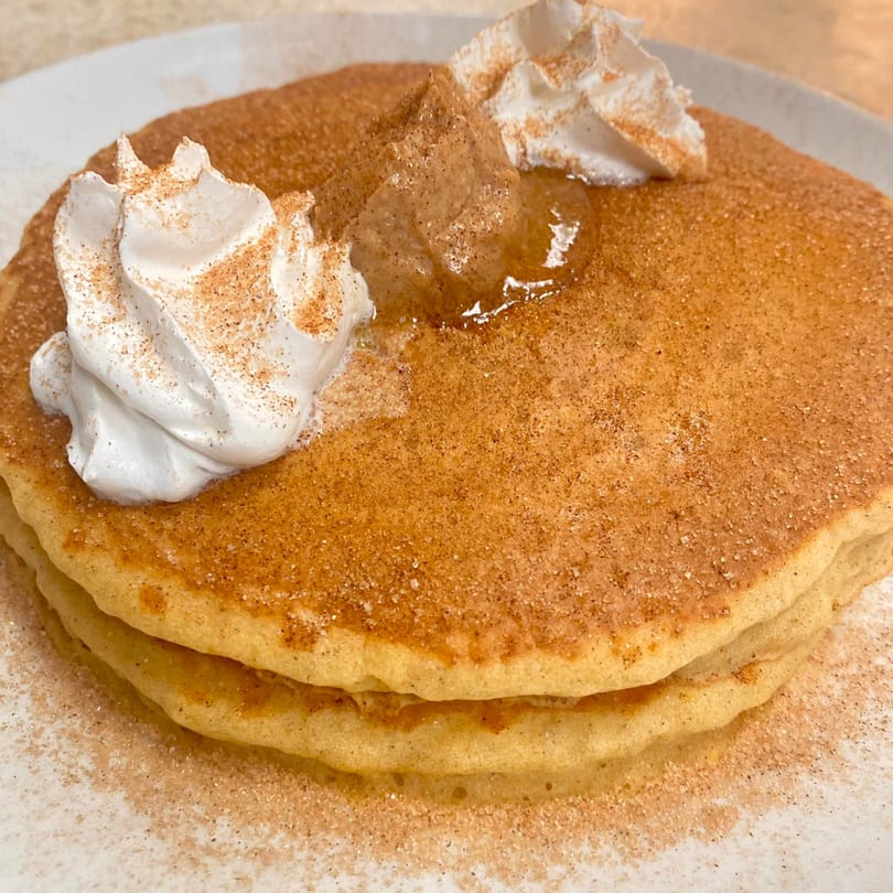Stack of cinnamon sugar pancakes with whipped cream, butter, and syrup on a white plate.