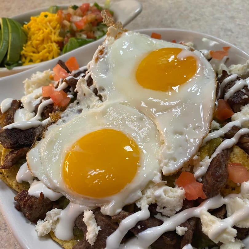Two sunny-side-up eggs on a bed of steak, cheese, tomatoes, and a side salad.