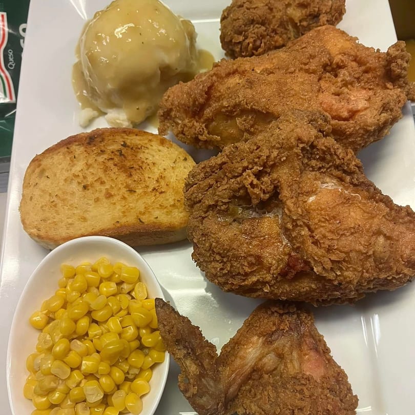 A plate of crispy fried chicken, mashed potatoes with gravy, garlic bread, and corn.